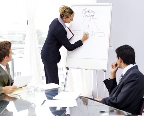 Businesswoman Writing on White Board and Businessman at Table